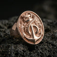 Load image into Gallery viewer, Sterling silver anchor and snake signet ring with a rose gold plated finish, raised anchor and coiled snake emblem, close-up on volcanic rock
