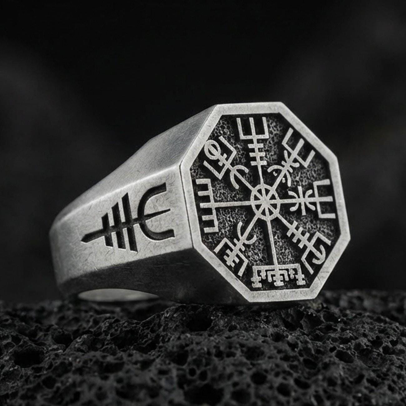Sterling silver Vegvisir signet ring with an oxidized finish, Viking runic compass engraved on an octagonal face, macro on black volcanic rock