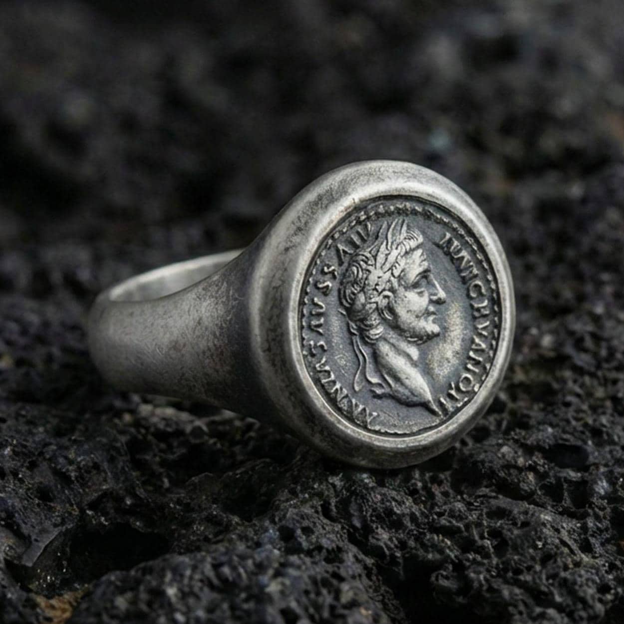 Sterling silver Roman coin signet ring with an oxidized finish, ancient emperor profile medallion with Latin-style lettering, macro on black volcanic rock