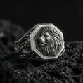 Load image into Gallery viewer, Oxidized sterling silver lion signet ring on volcanic rock, octagon face with raised lion head relief and deep textured background, macro studio photo
