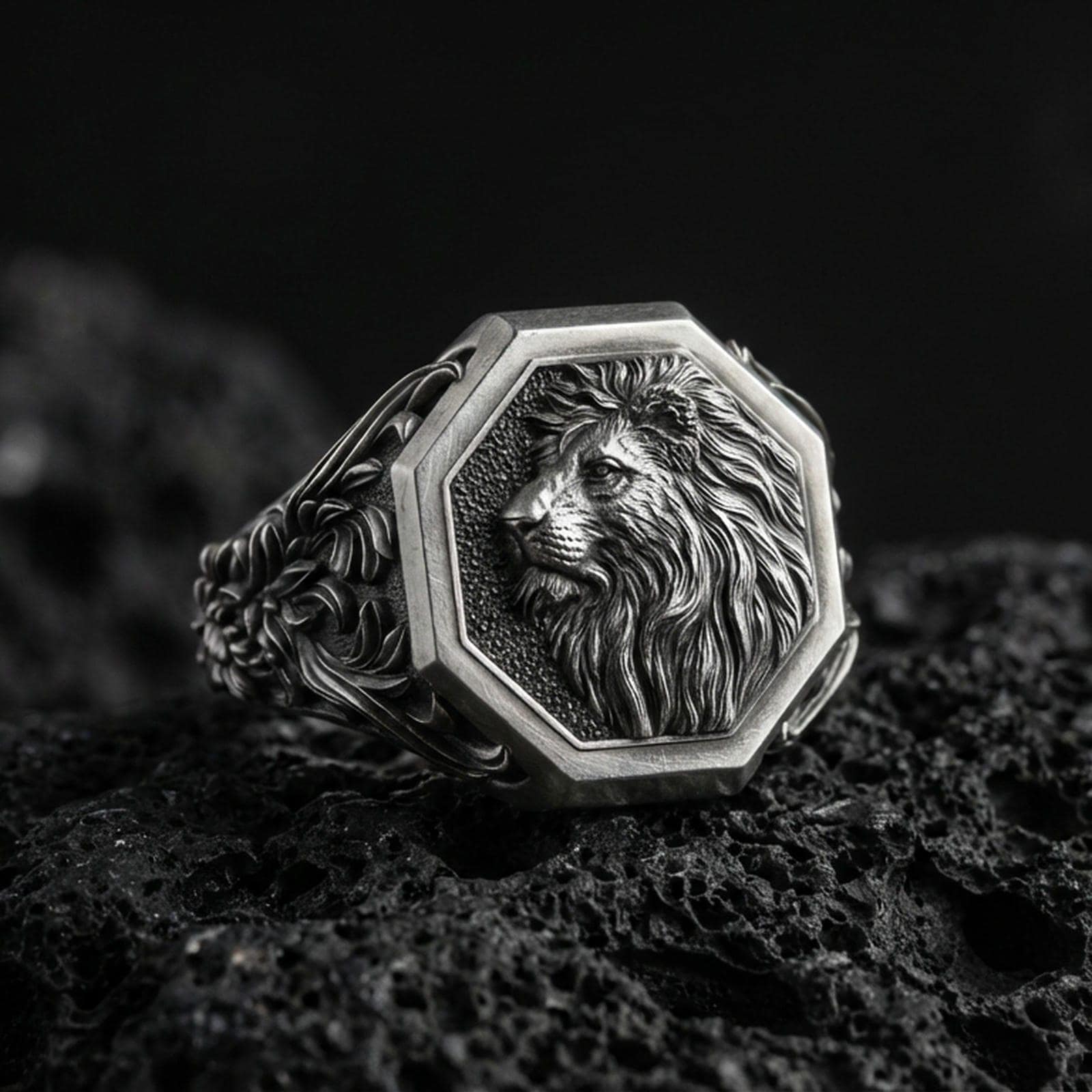 Oxidized sterling silver lion signet ring on volcanic rock, octagon face with raised lion head relief and deep textured background, macro studio photo