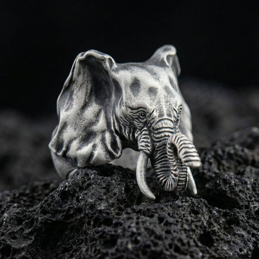 Oxidized sterling silver elephant ring on textured volcanic rock, close-up studio shot with premium dark background