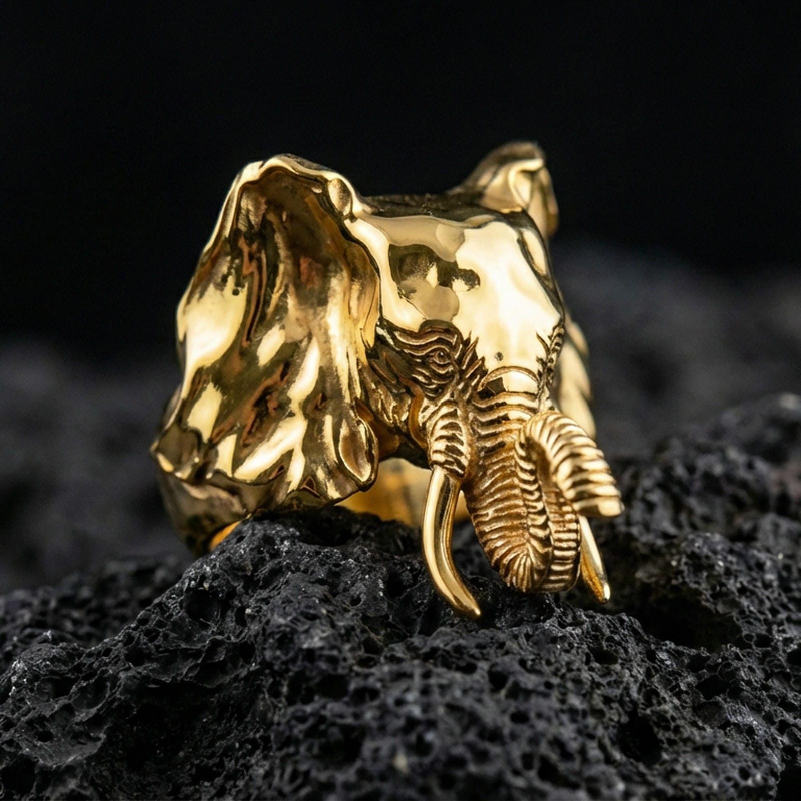 Gold plated elephant ring on porous volcanic stone, luxury studio lighting emphasizing sculpted face texture