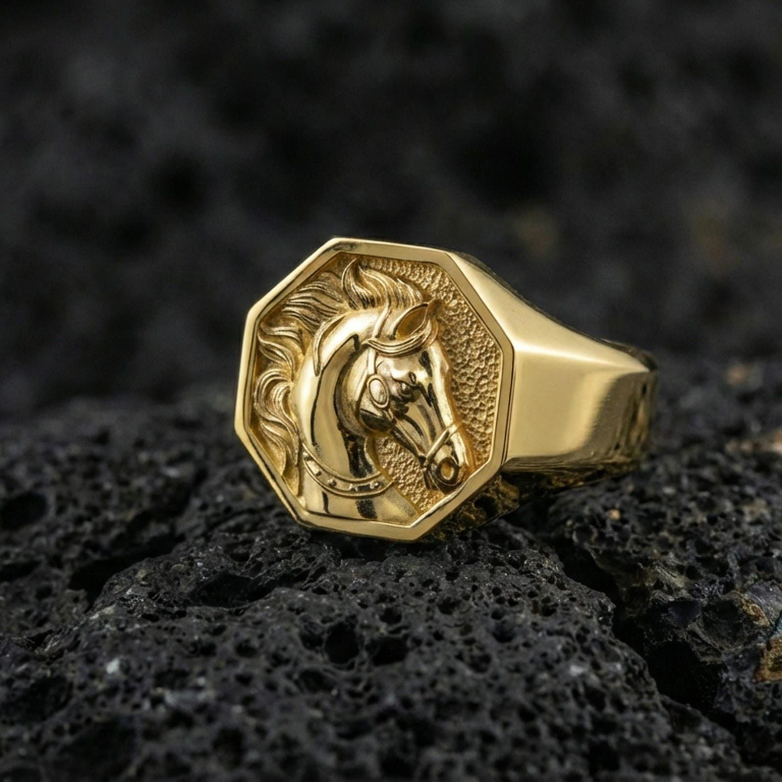 Gold plated horse signet ring on porous volcanic stone, premium dark background emphasizing the carved equestrian profile