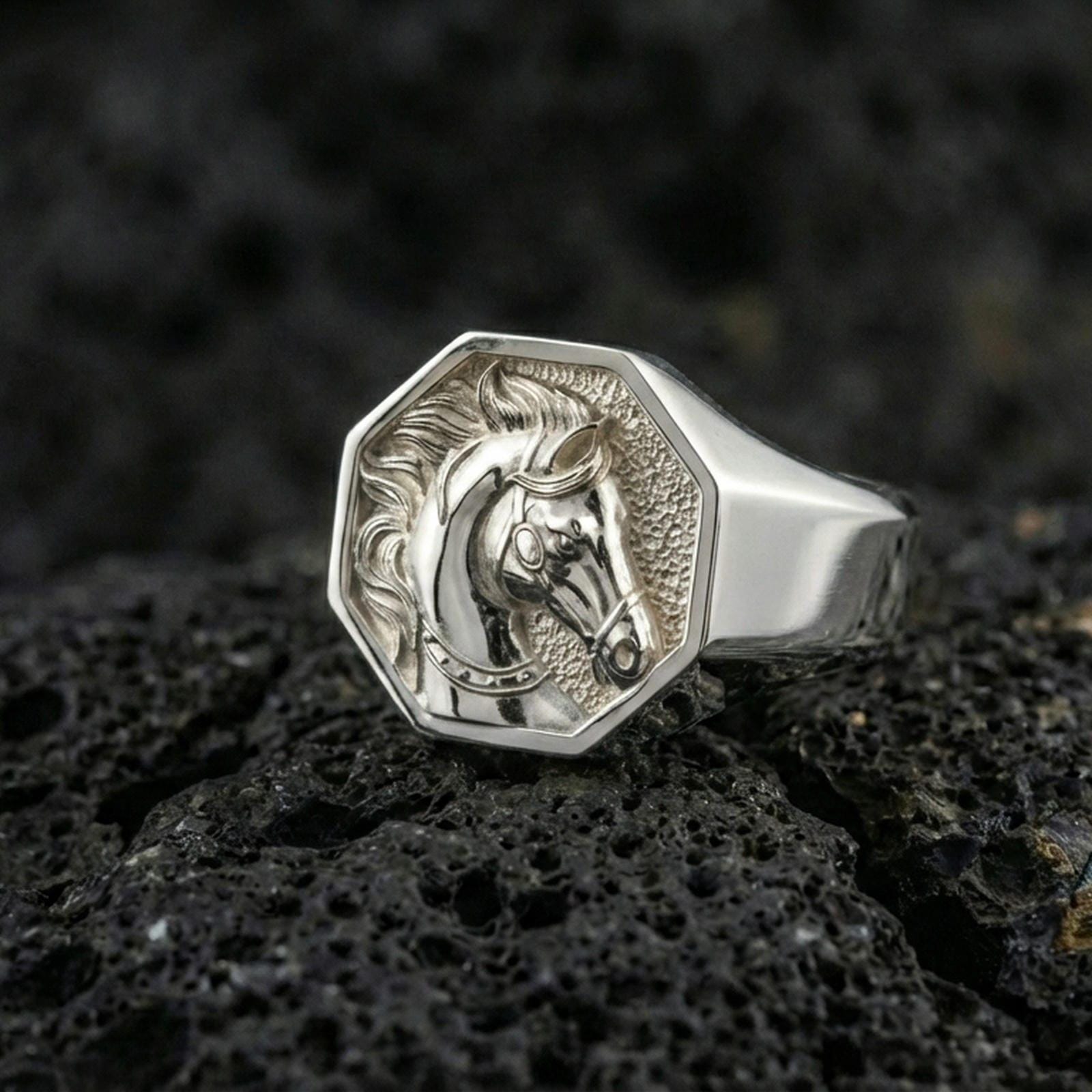 Polished silver horse signet ring on volcanic rock surface, close-up highlighting engraved mane details and clean geometric bezel