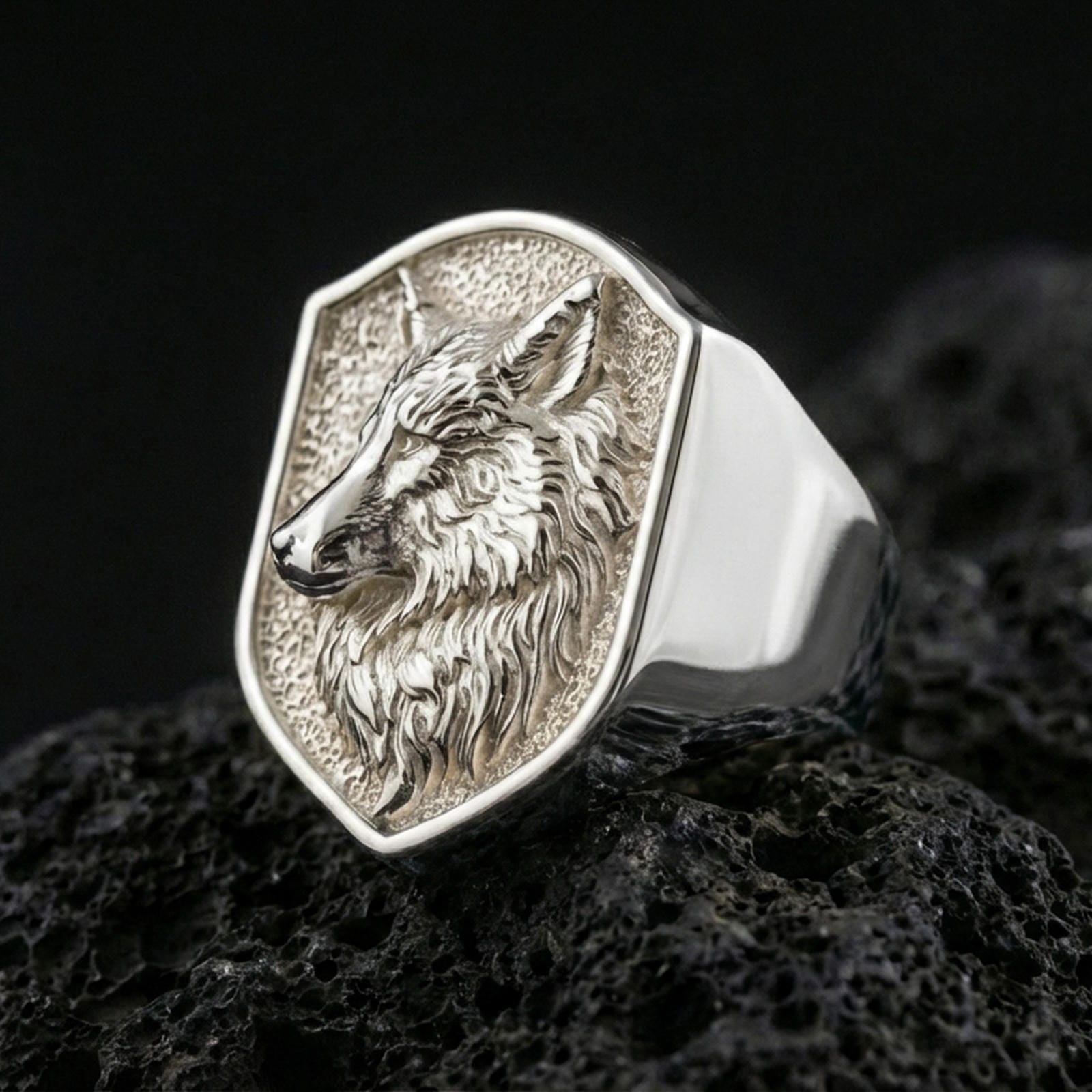 Polished silver wolf head signet ring on volcanic rock surface, studio close-up highlighting crisp bezel edges and realistic animal relief