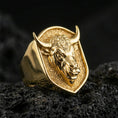 Load image into Gallery viewer, Gold plated bull signet ring on porous volcanic stone, premium dark background emphasizing the horns and sculpted animal portrait
