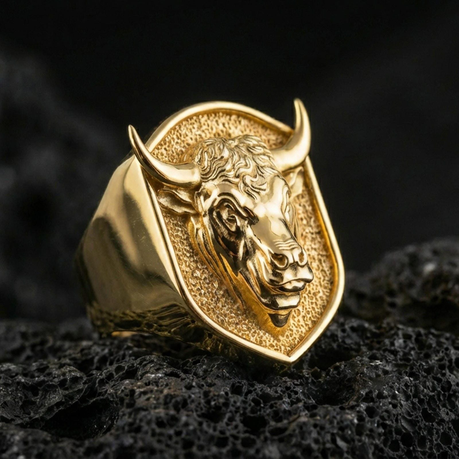 Gold plated bull signet ring on porous volcanic stone, premium dark background emphasizing the horns and sculpted animal portrait