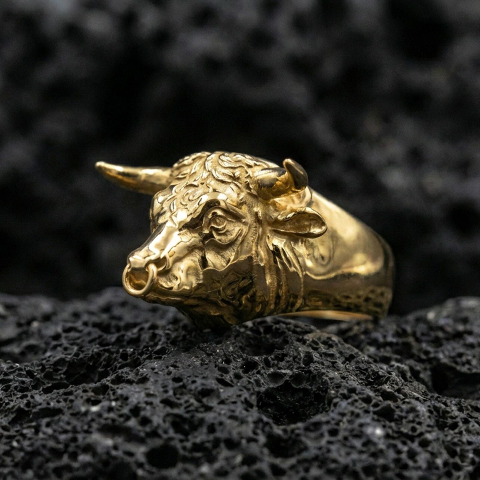 Gold plated bull head ring on porous volcanic stone, premium studio shot emphasizing the horned animal head and bold silhouette