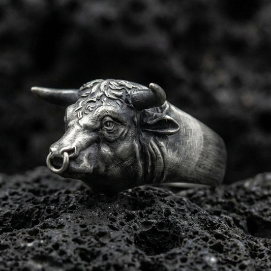 Oxidized sterling silver bull head ring on textured volcanic rock, macro close-up showing horns and nose ring detail in dark studio lighting