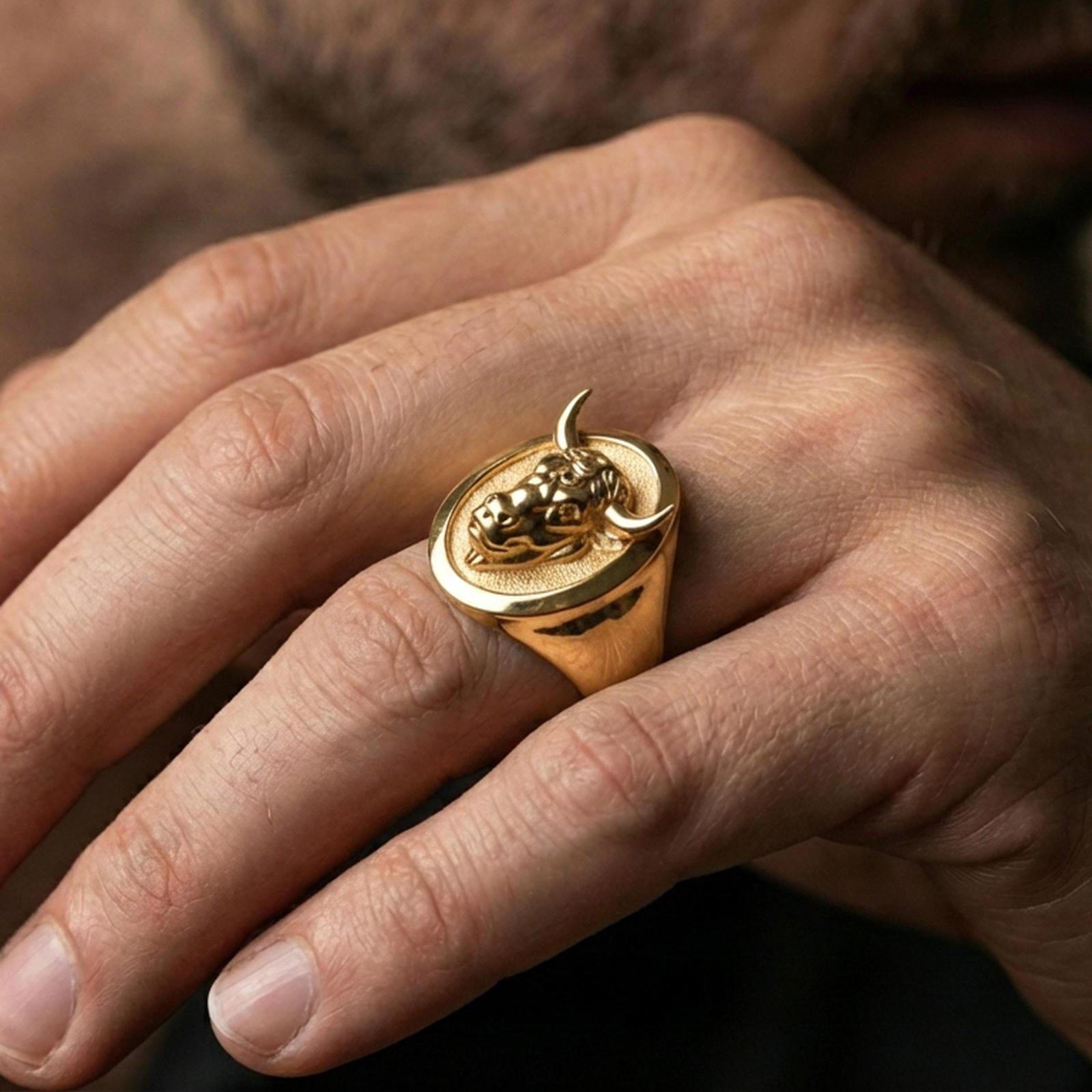 Gold plated bull signet ring worn on finger, lifestyle wear shot emphasizing the bold horned portrait and strong statement look