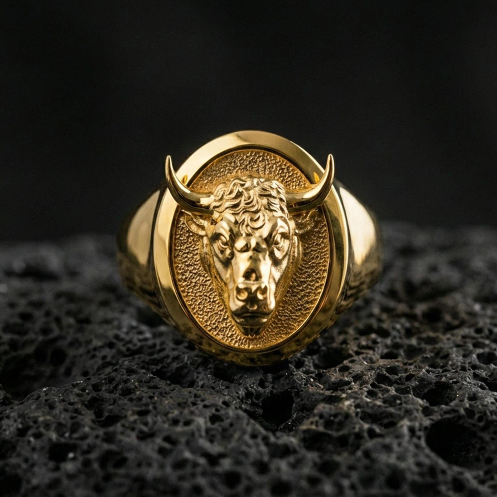 Gold plated bull signet ring on porous volcanic stone, premium dark background emphasizing the horns and bold animal portrait