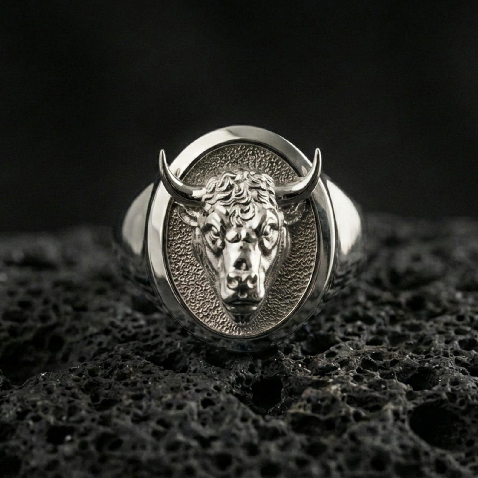 Polished silver bull head signet ring on volcanic rock surface, close-up highlighting the oval bezel and sculpted facial details