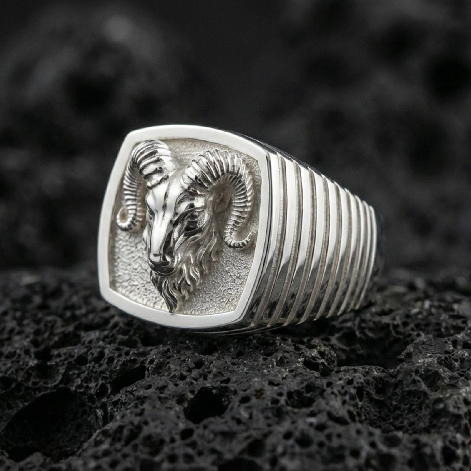 Polished silver ram head ring on volcanic stone, detailed horns and textured background
