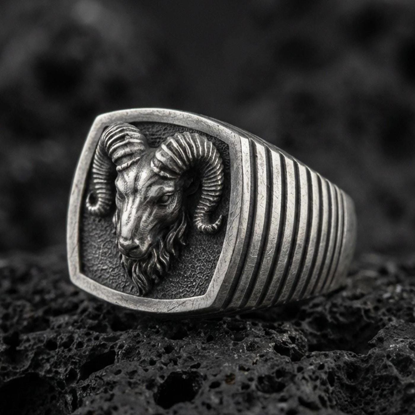 Oxidized sterling silver ram signet ring on volcanic rock, horned head shield face closeup