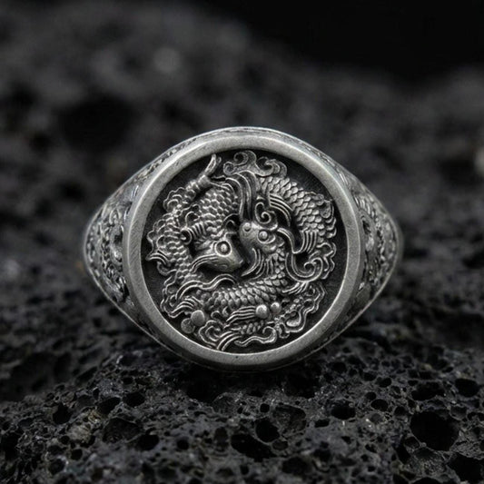 Oxidized sterling silver koi fish signet ring on textured volcanic rock, macro close-up showing detailed Japanese-inspired scales and swirling water relief