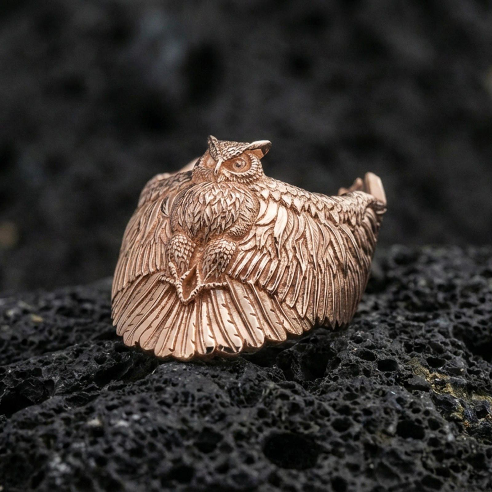 Rose gold plated owl ring on volcanic rock, sharp macro product photo showcasing the owl with outstretched wings and detailed feather pattern