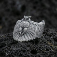 Load image into Gallery viewer, Oxidized sterling silver owl ring on textured volcanic rock, macro close-up showing spread wings, feather engraving, and intense owl eyes
