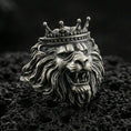 Load image into Gallery viewer, Oxidized sterling silver crowned lion ring on textured volcanic rock, macro close-up showing roaring lion head, detailed mane, and royal crown
