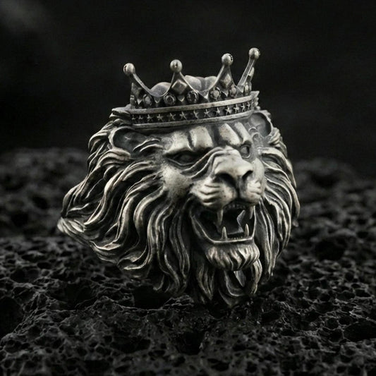 Oxidized sterling silver crowned lion ring on textured volcanic rock, macro close-up showing roaring lion head, detailed mane, and royal crown