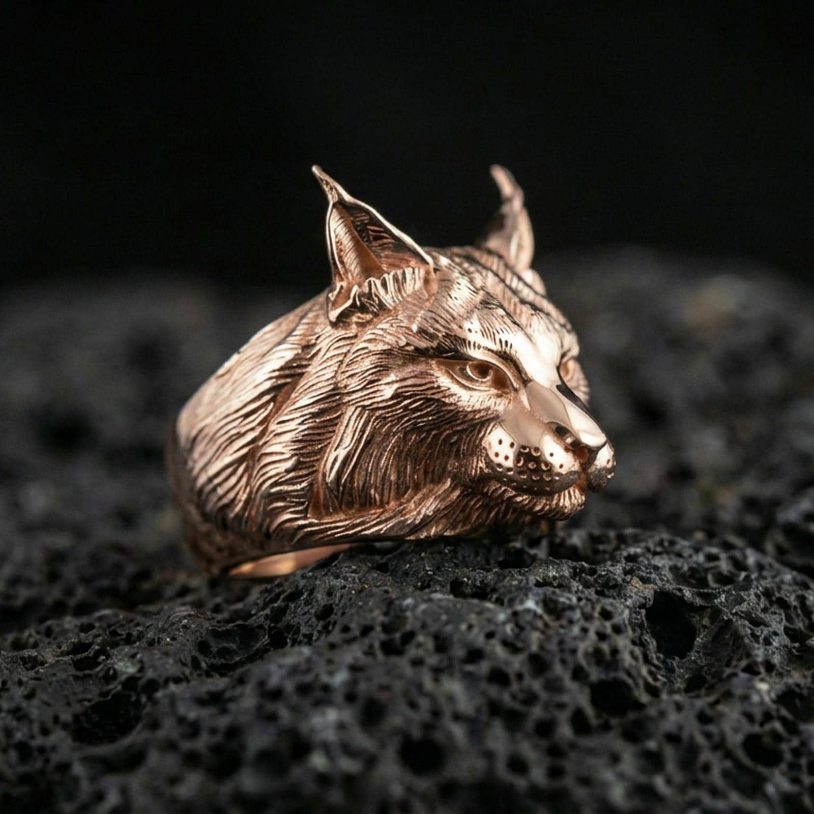 Rose gold plated lynx head ring on volcanic rock, sharp macro product photo showcasing the realistic feline profile and detailed fur pattern