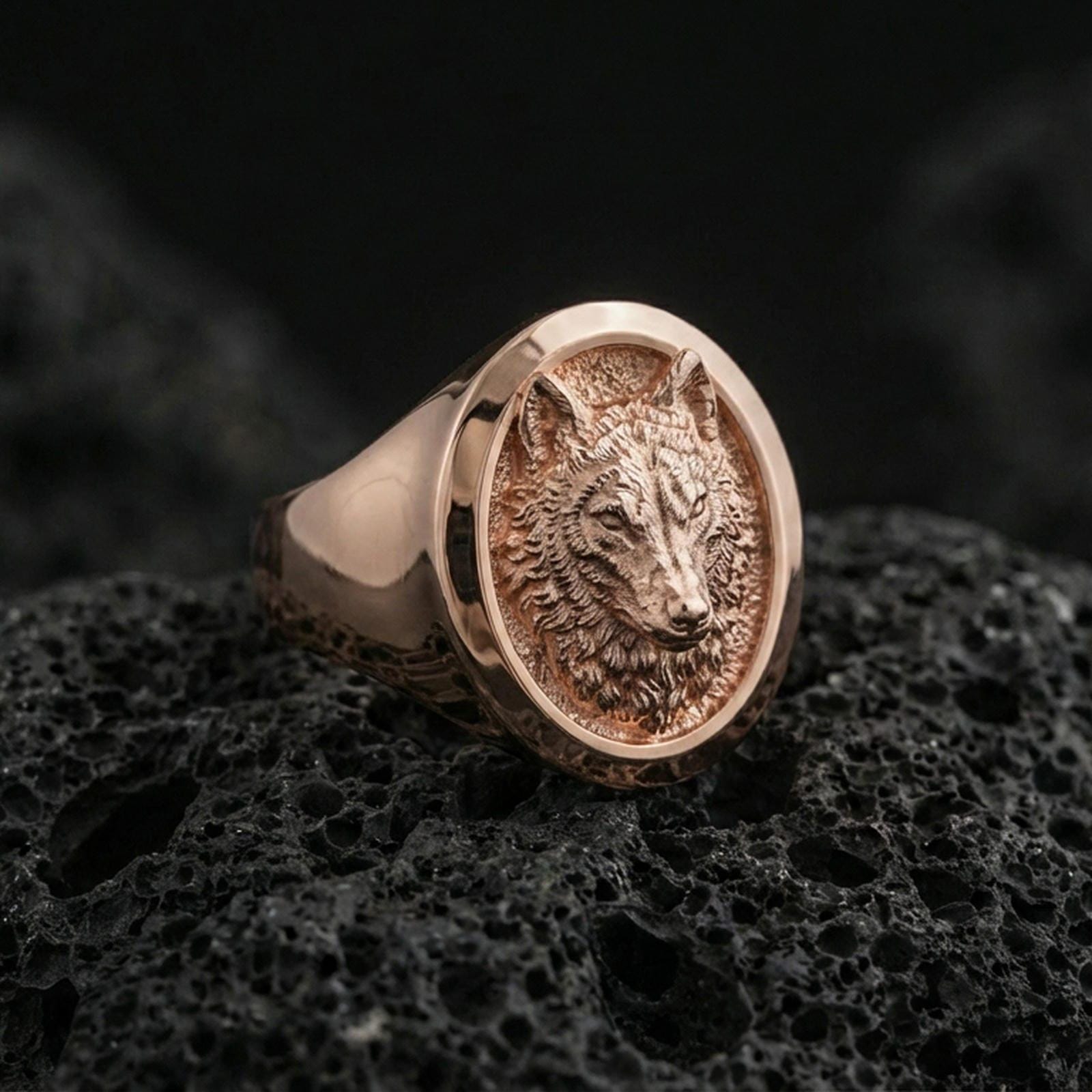 Rose gold plated wolf signet ring on volcanic rock, detailed wolf portrait with textured background