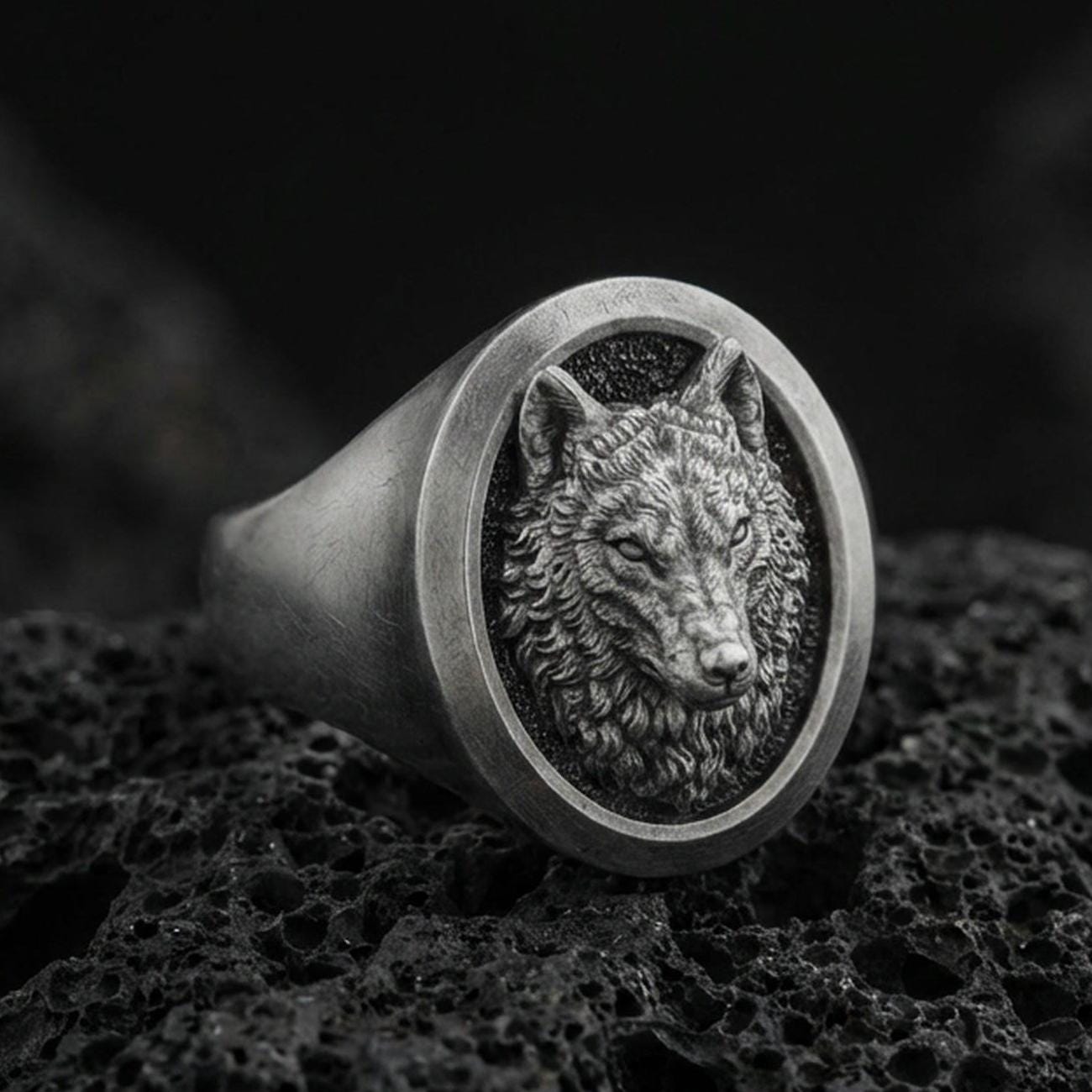 Oxidized sterling silver wolf signet ring on volcanic rock, macro closeup with dark textured backdrop