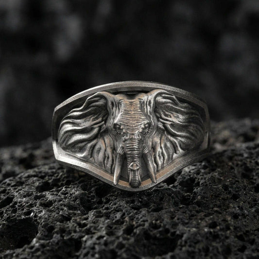 Oxidized sterling silver elephant signet ring on textured volcanic rock, macro close-up showing frontal elephant face, tusks, and flowing ear details