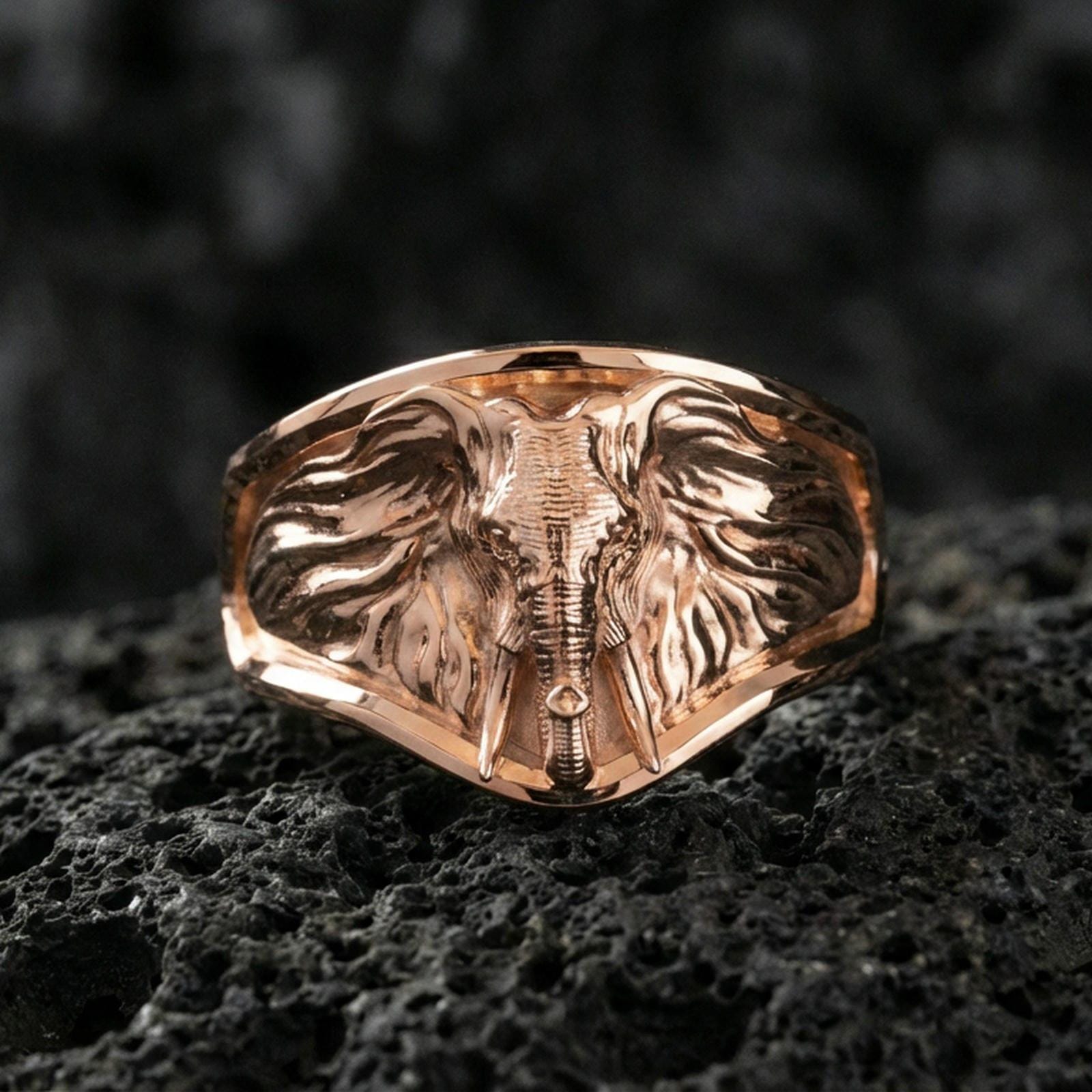 Rose gold plated elephant head ring on volcanic rock, sharp macro product photo showcasing the frontal elephant portrait and clean signet silhouette