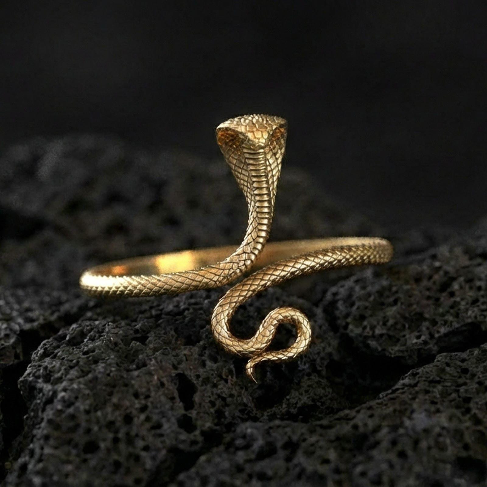 Gold plated cobra snake ring on porous volcanic stone, premium dark studio shot emphasizing the upright hood, curled tail, and realistic texture
