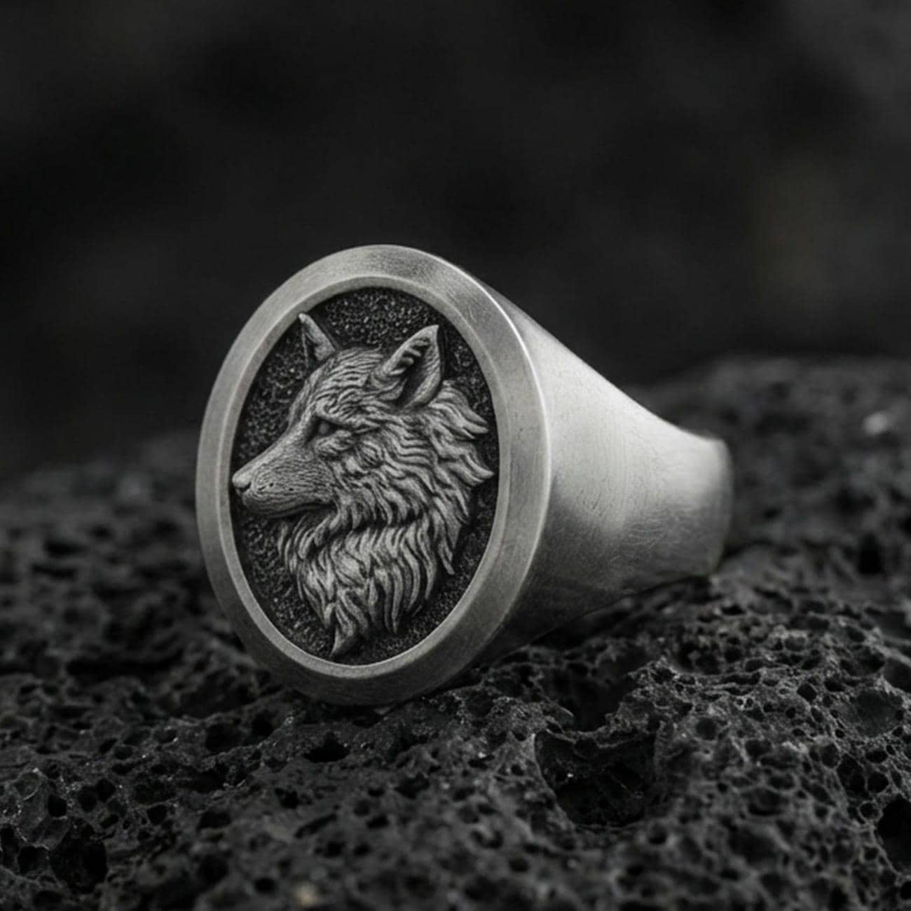 Oxidized sterling silver wolf signet ring on volcanic rock, macro closeup with deep shadow contrast
