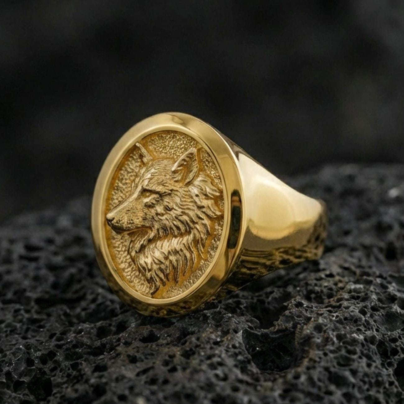 Gold plated wolf head ring on volcanic stone, bold animal emblem with crisp sculpted fur texture