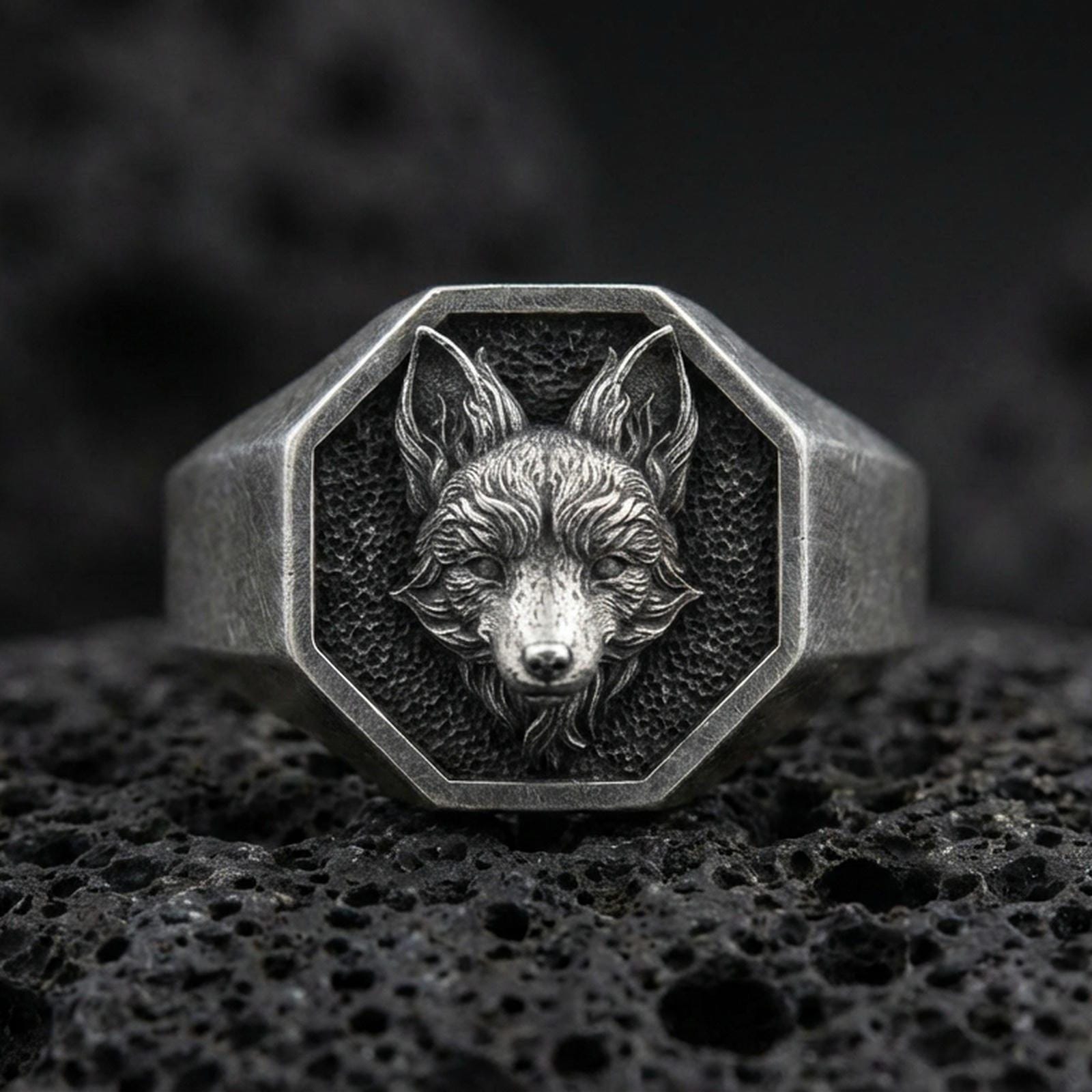 Close-up of an oxidized sterling silver fox signet ring centered on porous volcanic rock in a dark studio setting