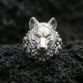 Load image into Gallery viewer, Front view of a polished silver wolf head ring on textured volcanic rock with premium macro lighting

