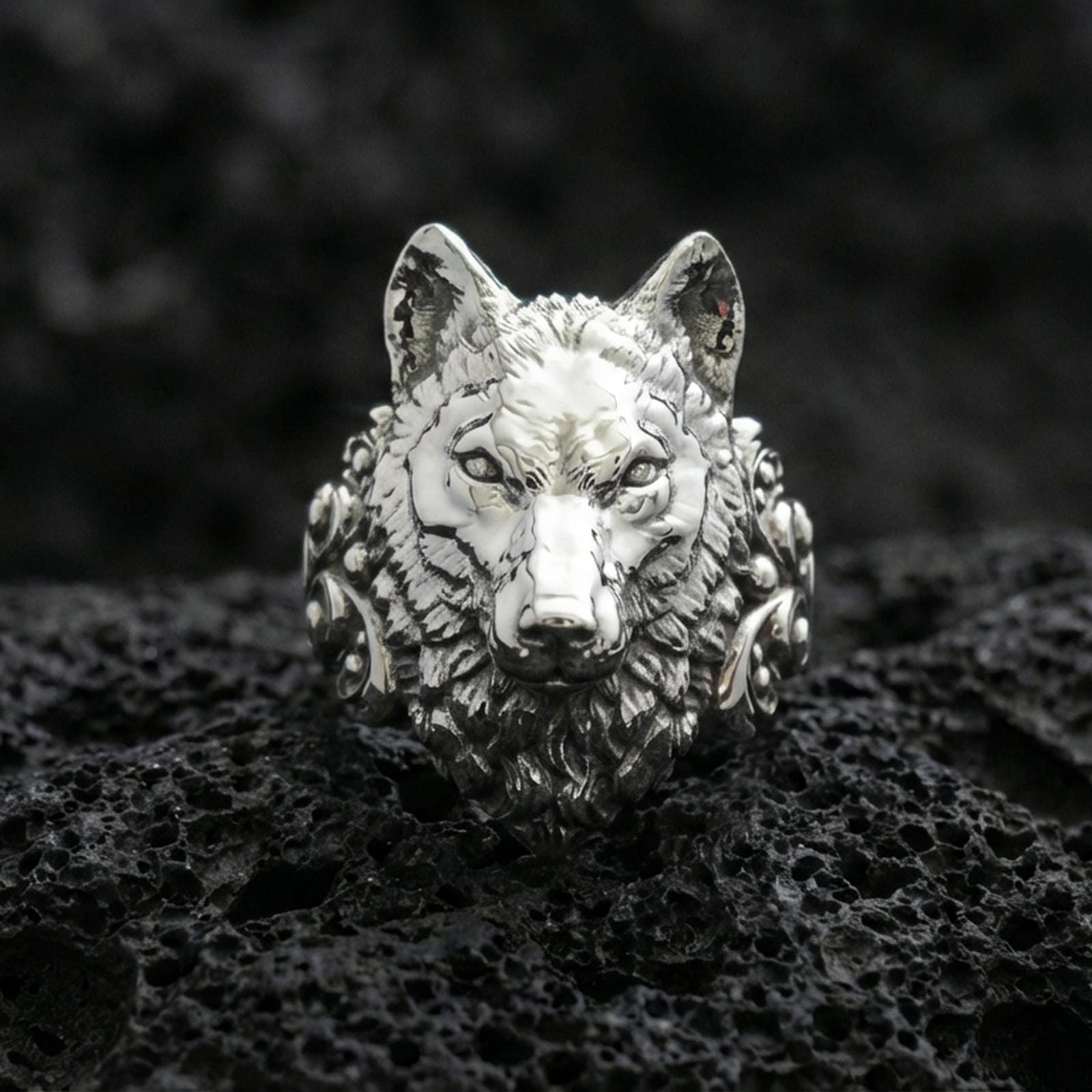Front view of a polished silver wolf head ring on textured volcanic rock with premium macro lighting