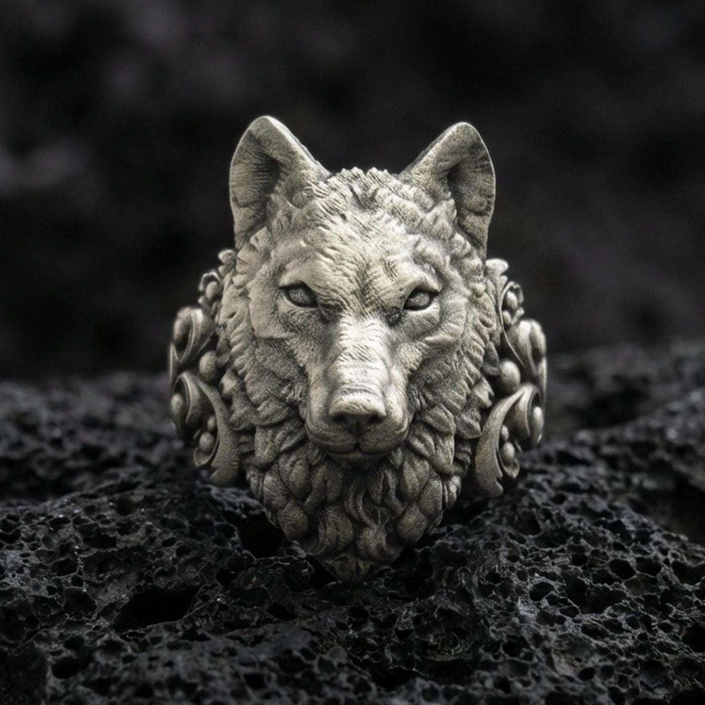 Close-up of an oxidized sterling silver wolf head ring centered on porous volcanic rock in a dark studio setting