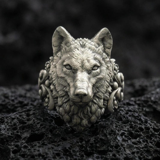 Close-up of an oxidized sterling silver wolf head ring centered on porous volcanic rock in a dark studio setting
