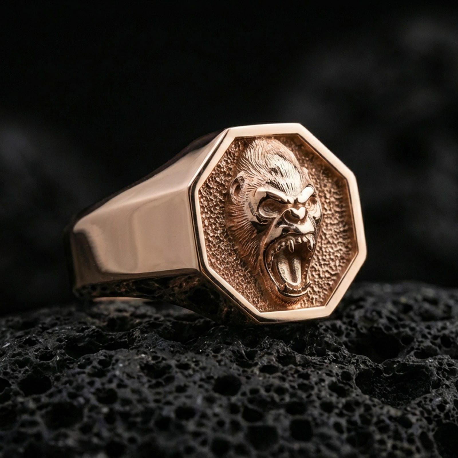 Rose gold plated gorilla signet ring on porous volcanic rock with dramatic shadows and sharp facial texture
