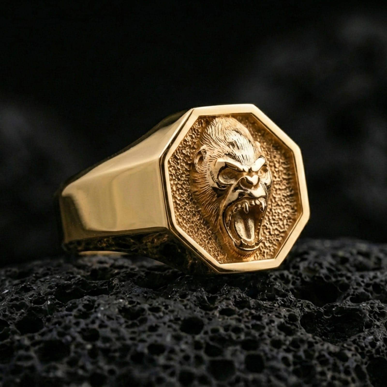 Gold plated octagon gorilla ring on black volcanic stone, close-up highlighting the roaring mouth and relief detail