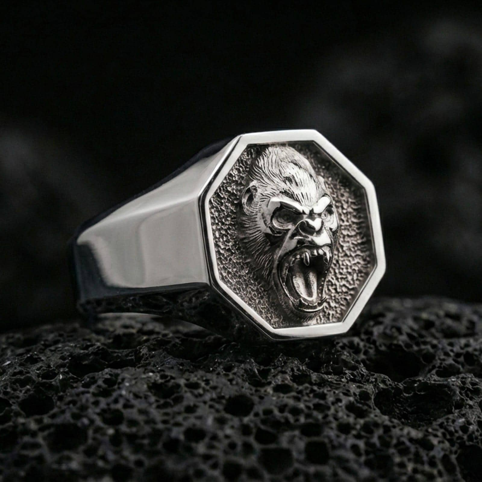 Polished silver gorilla signet ring displayed on textured volcanic rock with crisp macro focus and premium lighting