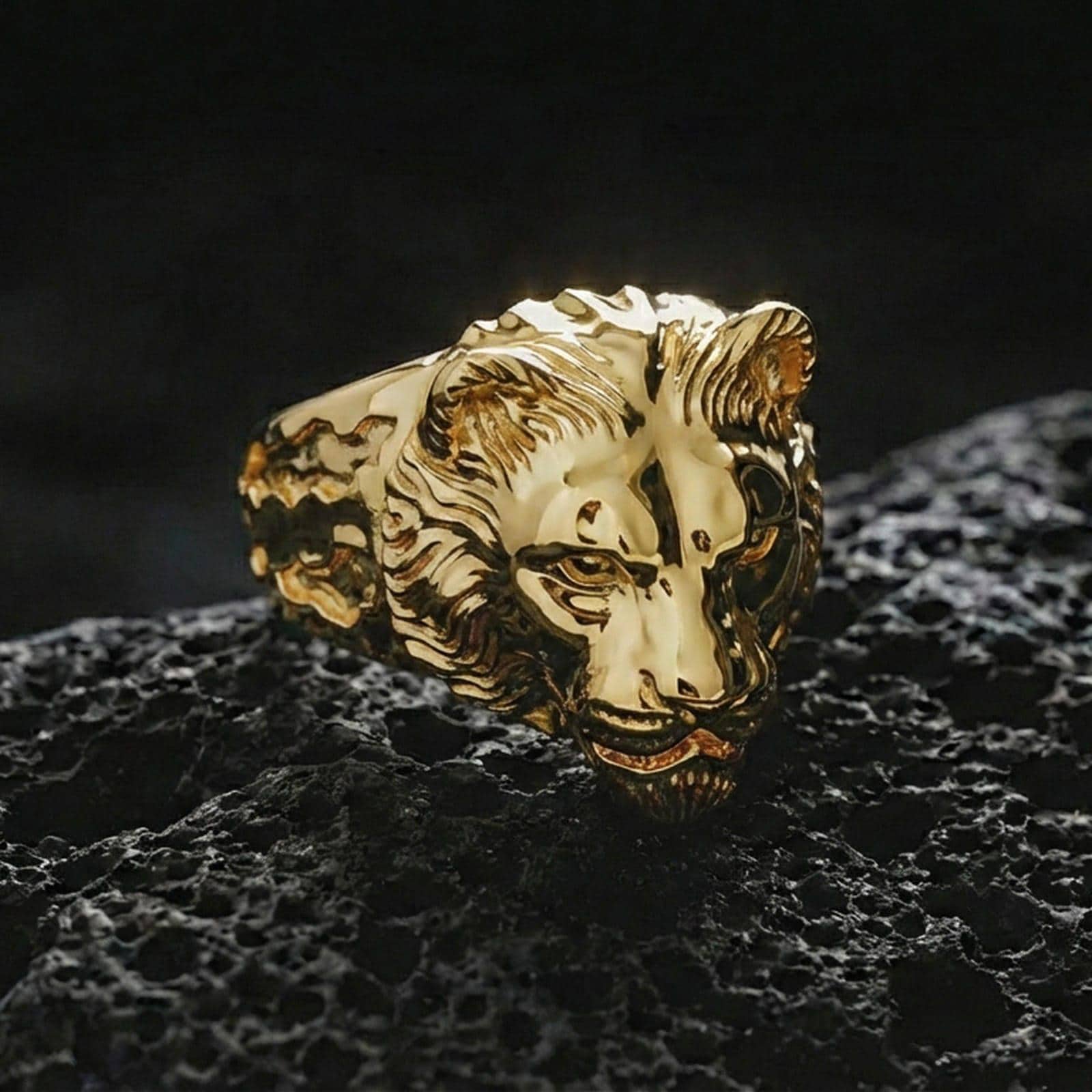 Gold plated lioness head ring on black volcanic stone, close-up highlighting the sculpted face and relief depth