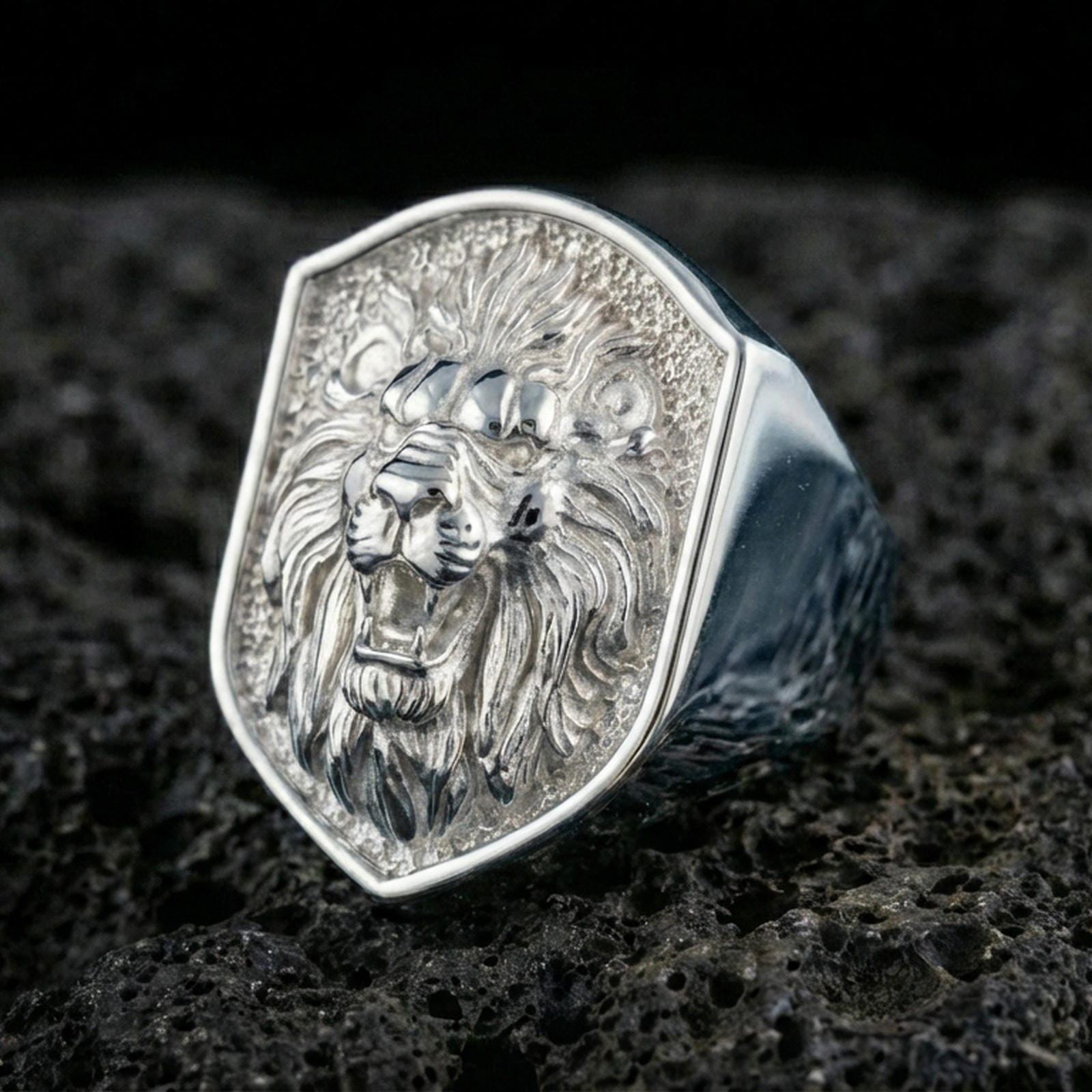 Polished silver lion signet ring on textured volcanic stone with sharp macro detail and soft directional lighting