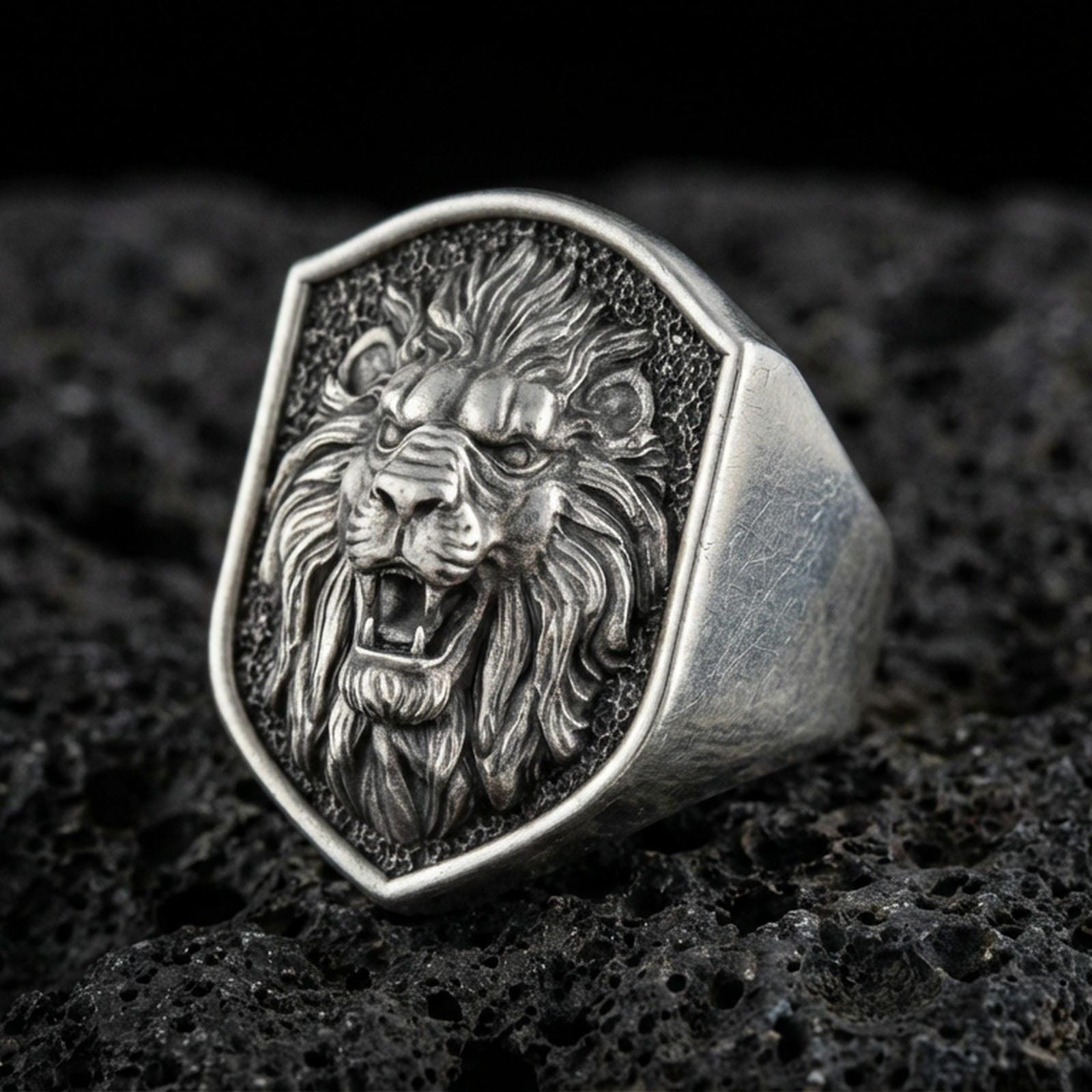 Close-up of an oxidized sterling silver roaring lion signet ring on porous volcanic rock in a dark studio setting