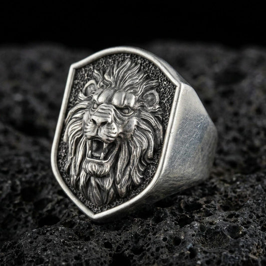 Close-up of an oxidized sterling silver roaring lion signet ring on porous volcanic rock in a dark studio setting