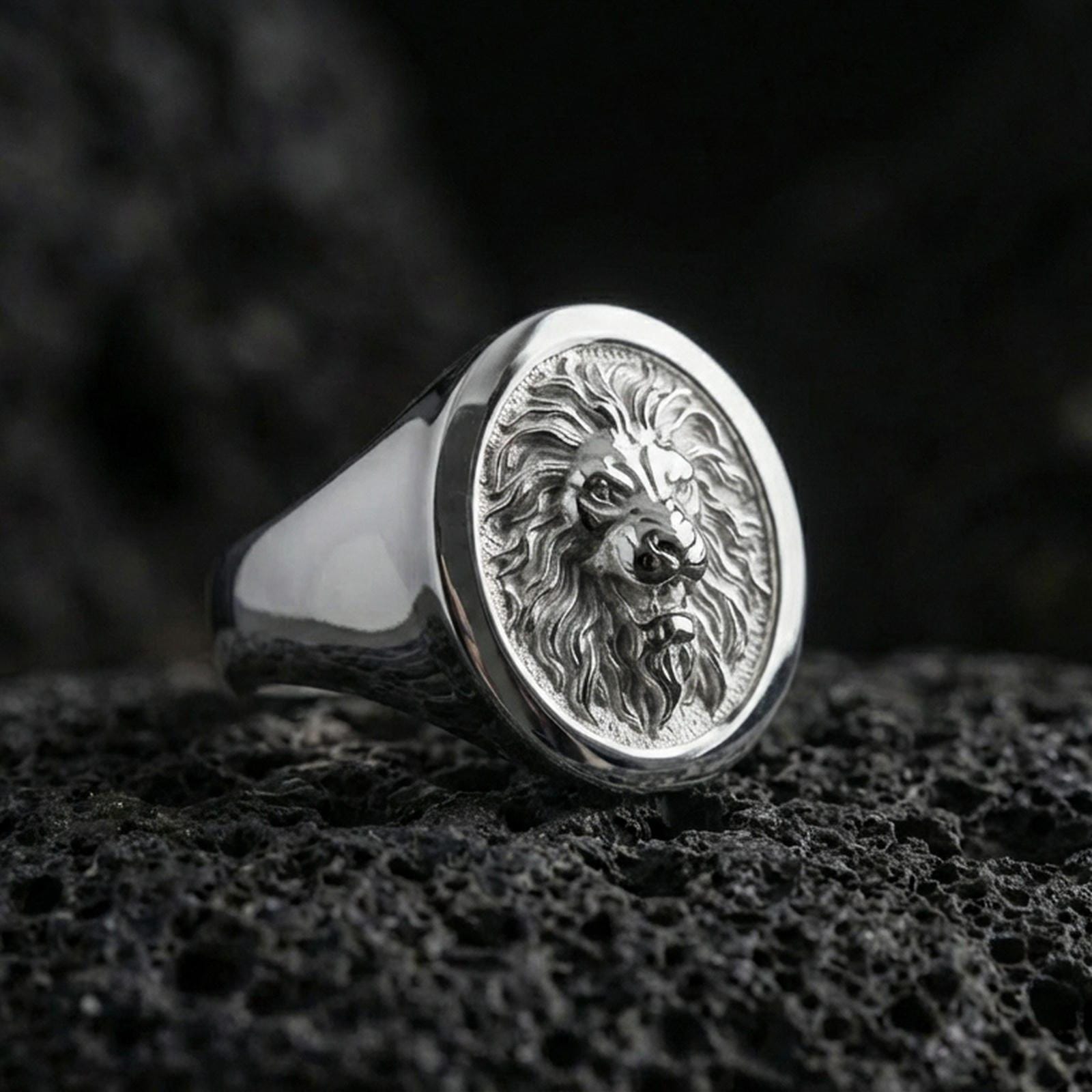 Polished silver lion signet ring on porous volcanic stone, close-up focusing on the crisp mane engraving and smooth round bezel edge