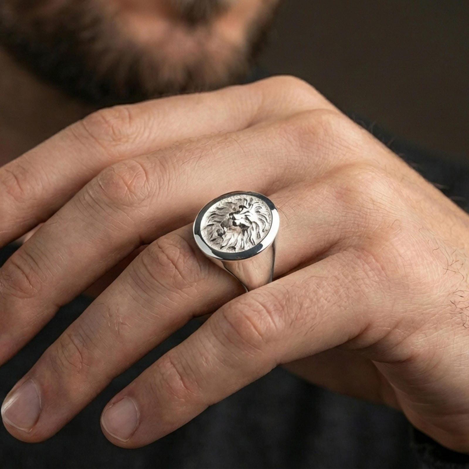Polished silver lion signet ring on finger, natural hand pose highlighting the detailed mane carving and clean round signet profile