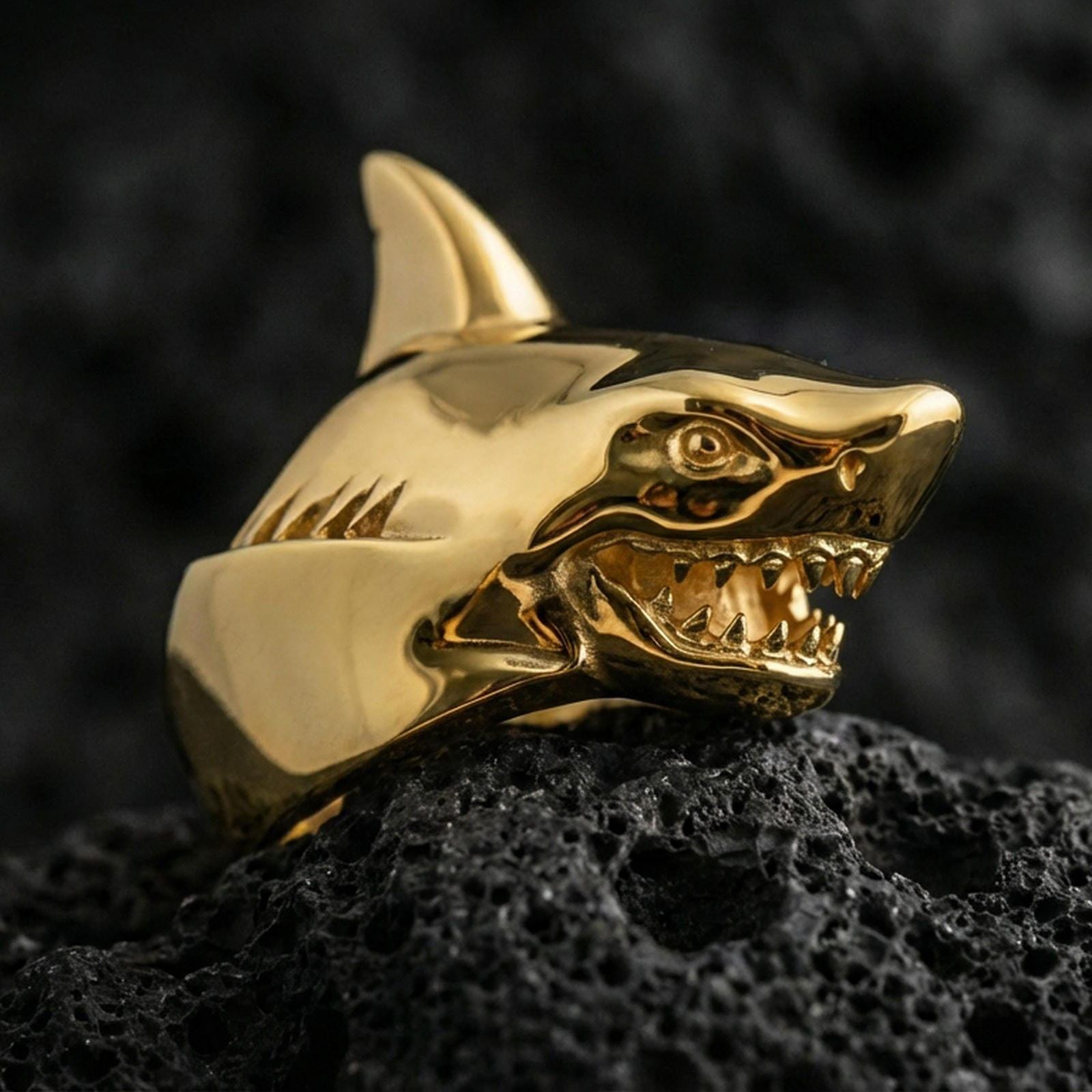 Gold plated shark head ring on black volcanic rock, close-up emphasizing the aggressive teeth and smooth contours