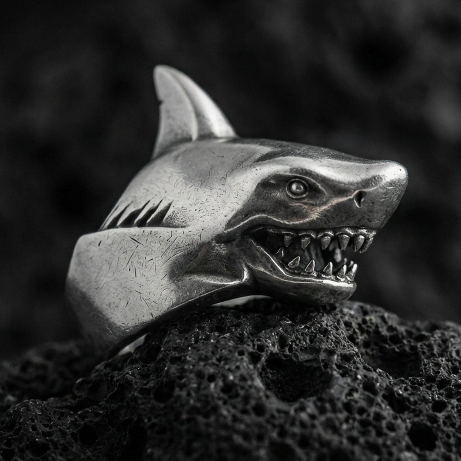 Close-up of an oxidized sterling silver shark head ring on porous volcanic rock in a dark studio setting