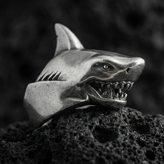 Close-up of an oxidized sterling silver shark head ring on porous volcanic rock in a dark studio setting