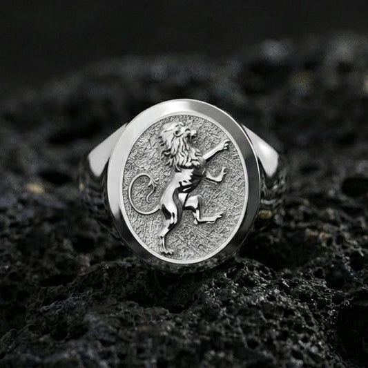 Polished silver royal lion signet ring on porous volcanic stone, close-up focusing on the crisp heraldic engraving and smooth round bezel edge